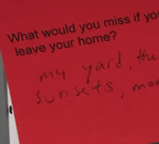 A red paper with printed text that reads, 'What would you miss if you leave your home?' and handwritten response, 'my yard, the sunsets, mom.'