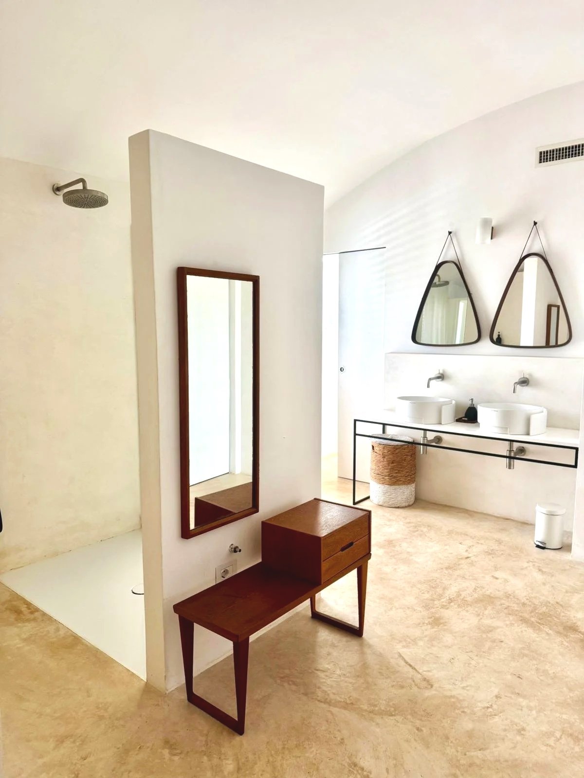 Salle de bain moderne avec deux lavabos ronds sur un comptoir blanc, deux miroirs triangulaires suspendus, un panier en osier, un meuble en bois et un grand miroir encadré en bois.