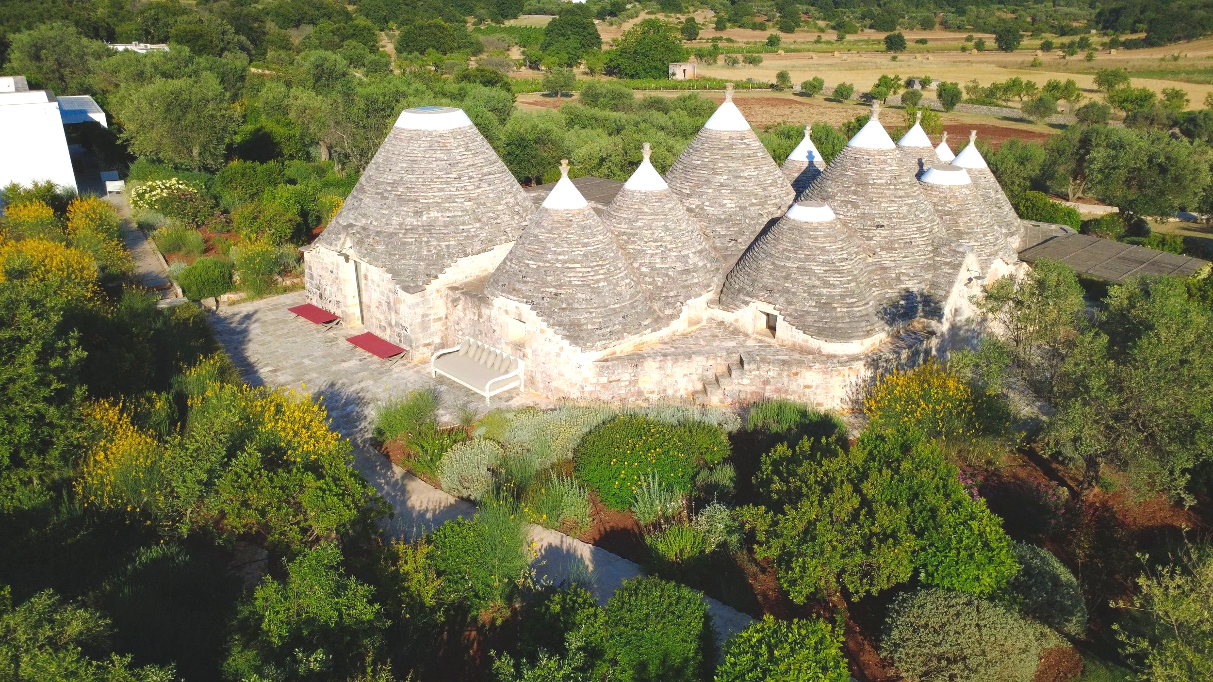 Vue aérienne d'un bâtiment avec un toit en forme de cône en pierre, entouré de végétation verdoyante.