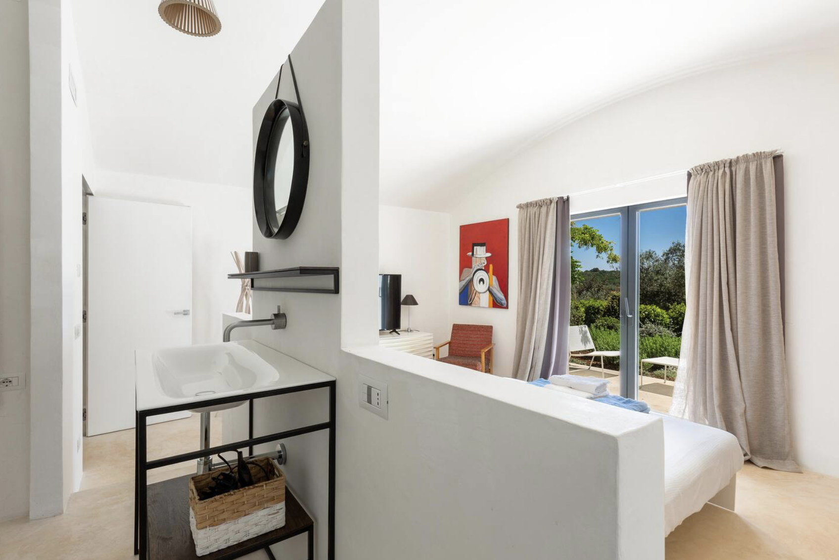 vue d'une chambre avec un lit à baldaquin, des fenêtres ouvertes avec des rideaux beige, une fresque moderne sur le mur et un coin salon avec une lampe