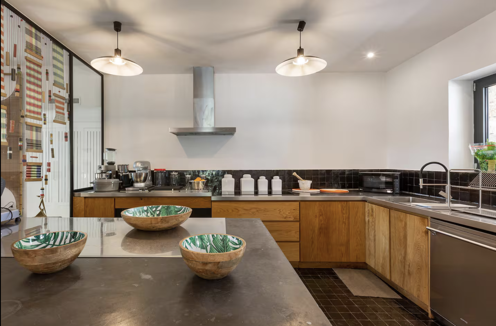 Cuisine moderne avec des armoires en bois, comptoir en pierre, étagères en verre avec livres, et divers appareils électroménagers, vue d'ensemble élégante et lumineuse.