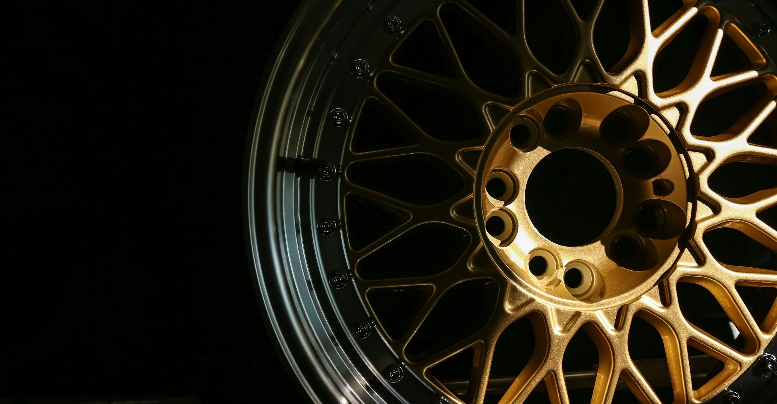 Close-up of a gold-colored motorcycle wheel with intricate spokes and black lug nuts, against a black background.