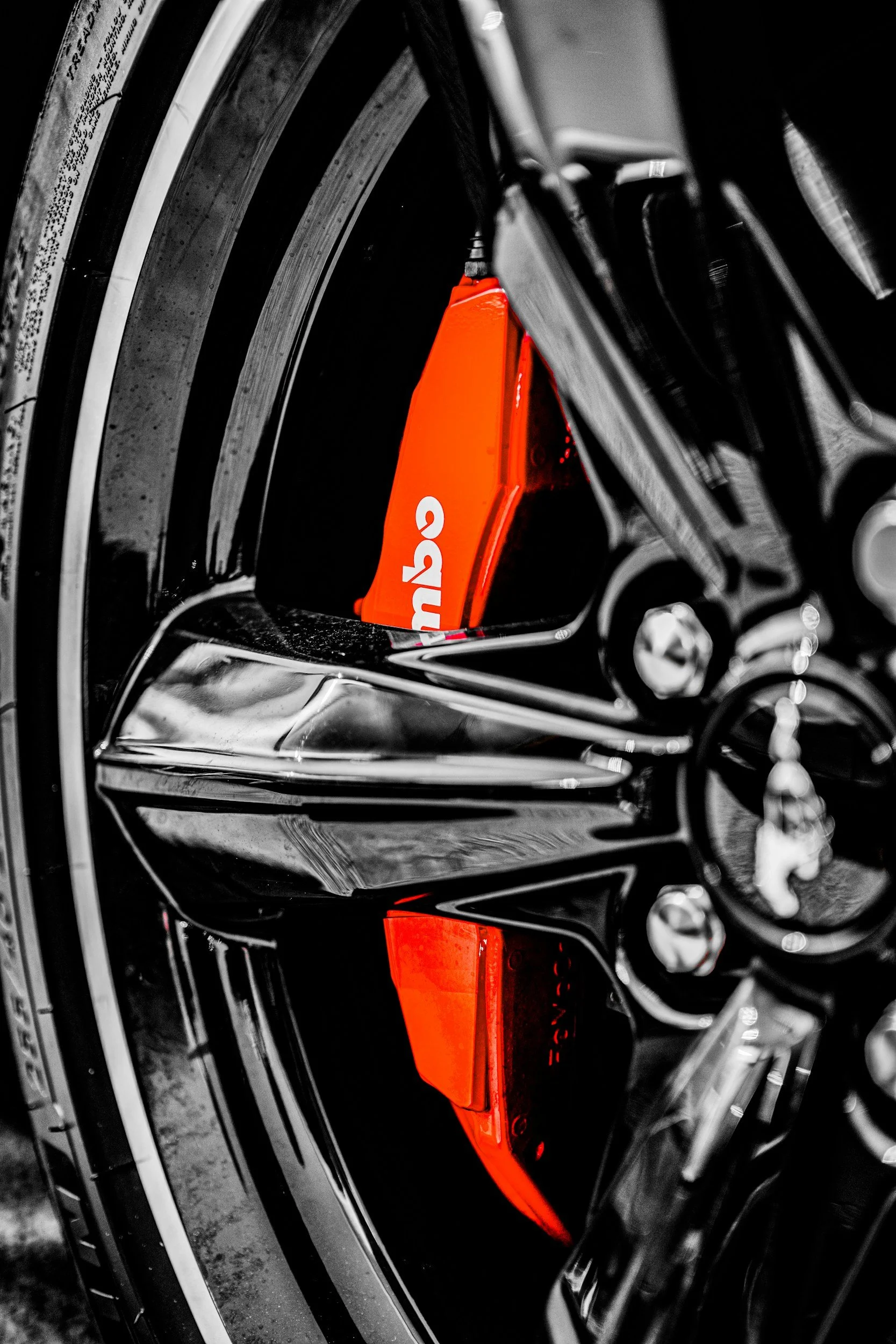 Close-up of a car wheel with a brake caliper painted in bright orange, with the brand name partially visible in white letters.
