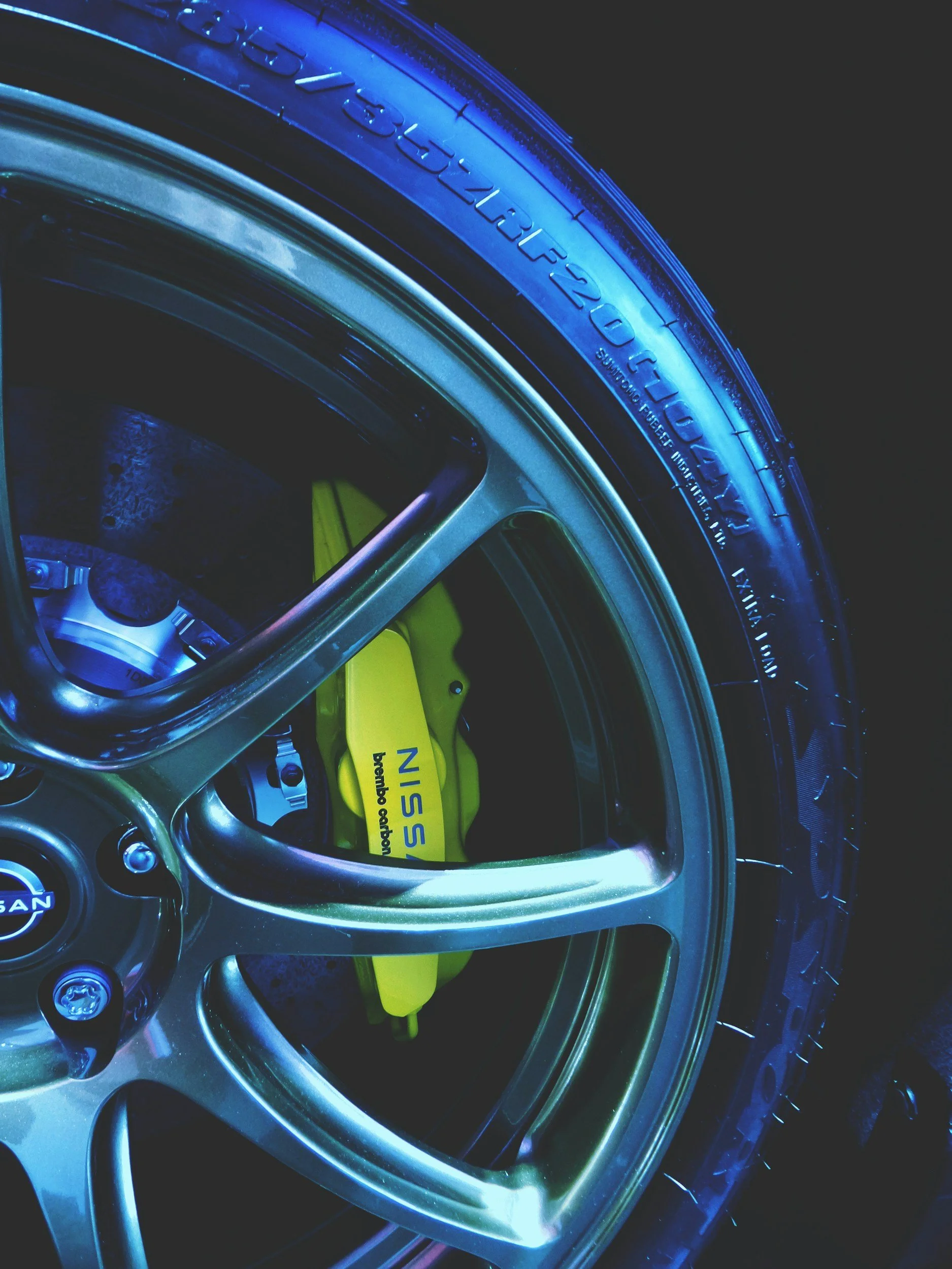 Close-up of a car wheel with a Nissan logo, yellow high-performance brake calipers, and tire.
