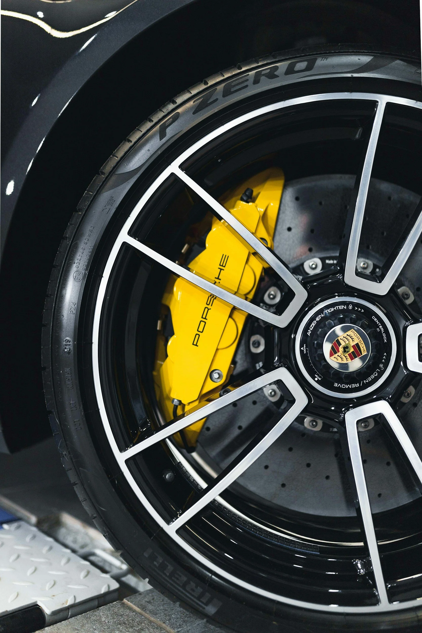 Close-up of a black sports car wheel with a Porsche logo on the center cap, yellow brake caliper, and high-performance tire.
