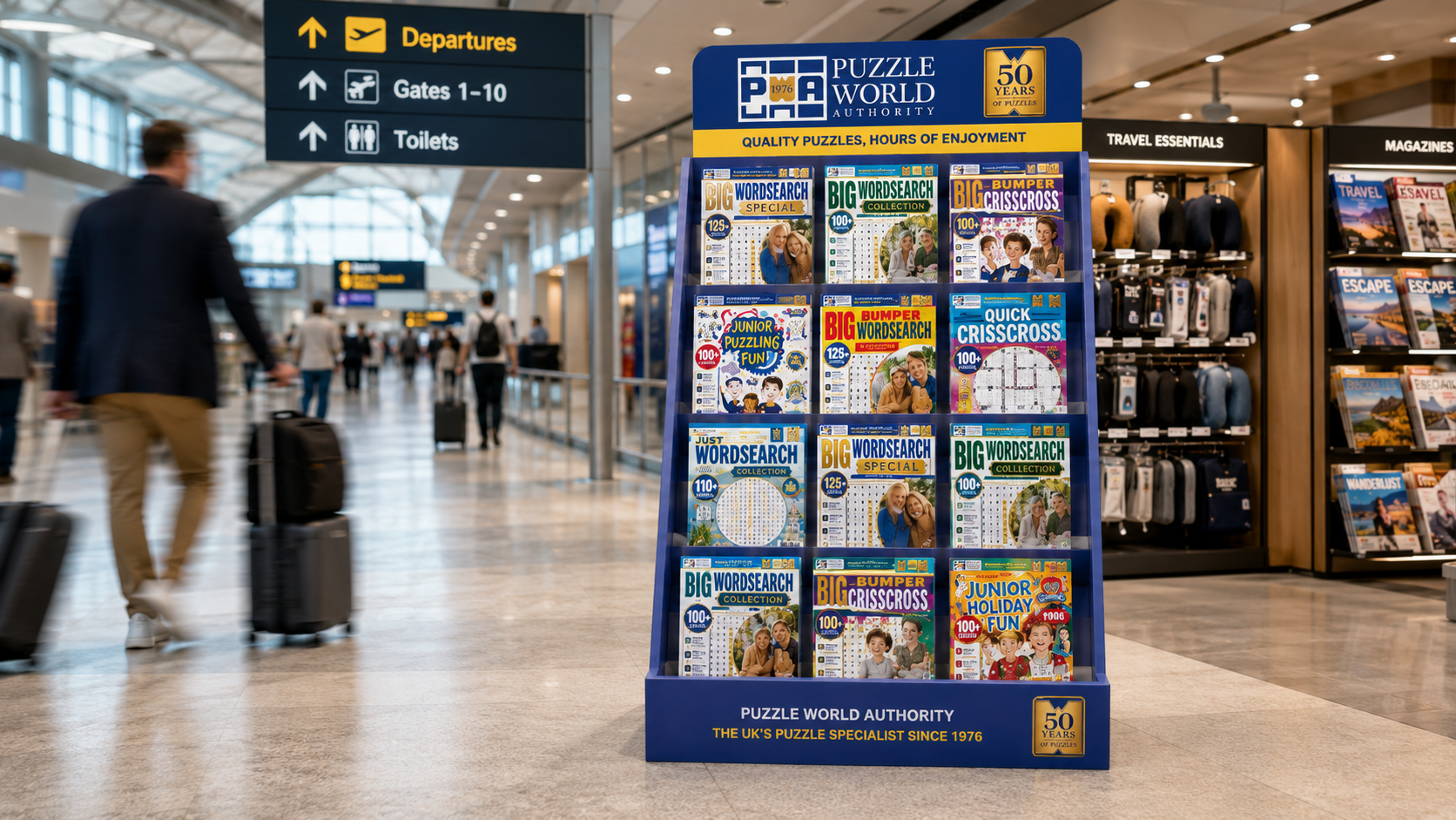 A display rack of puzzle books at an airport terminal. The rack features various puzzle book titles, including word search, crossword, and junior puzzle books. Signage overhead indicates directions to departures, gates, and toilets, with people walking in the background.