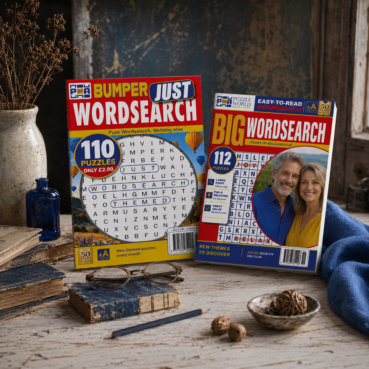 Two puzzle books titled 'Bumper Just Wordsearch' and 'Big Wordsearch' sit on a rustic wooden table, surrounded by old books, a pair of glasses, and decorative items like a dried flower arrangement, a small blue bottle, and a bowl of decorative balls. A pair of glasses rests on the table.