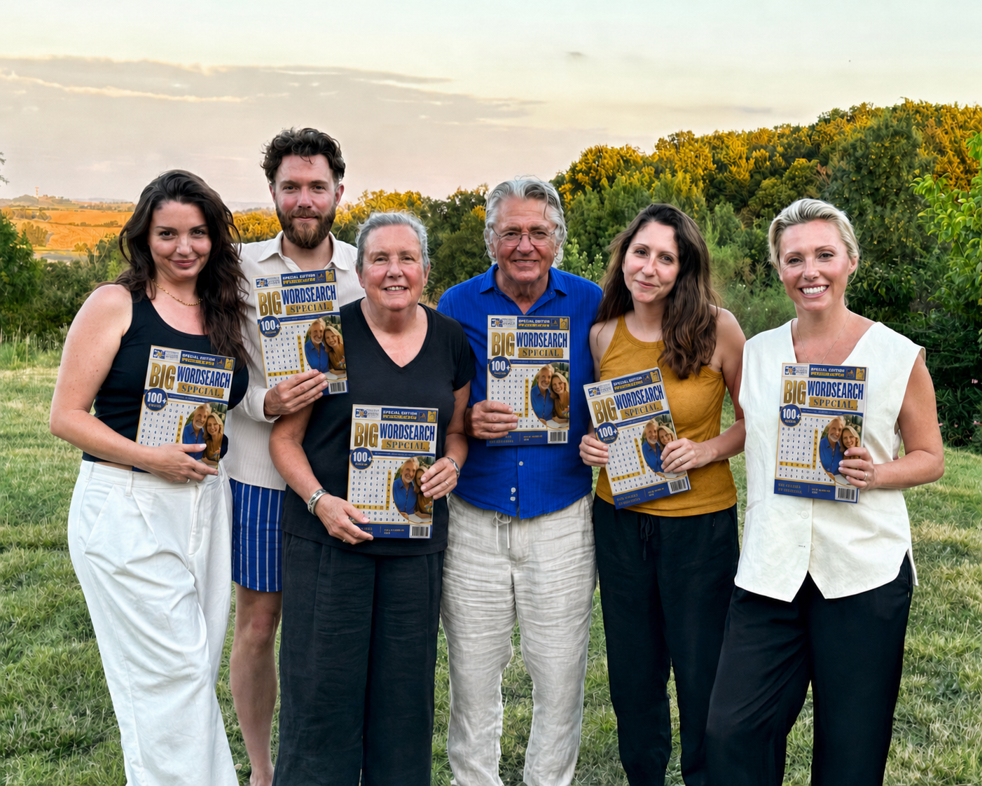 Seven people standing outdoors holding magazines titled 'Big WordSearch Special', with a lush background of trees and a sunset sky.