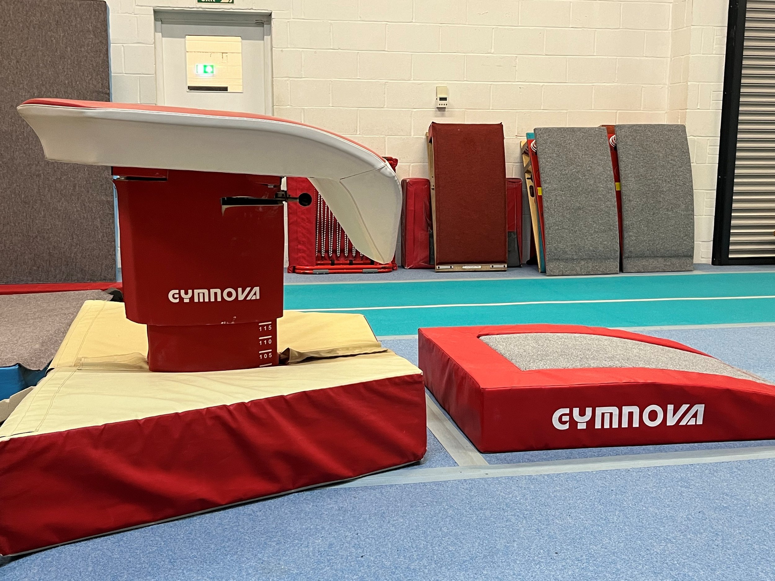 Gymnastics training area with red and yellow mats, a vaulting table, and cushioned platforms in a gymnasium.