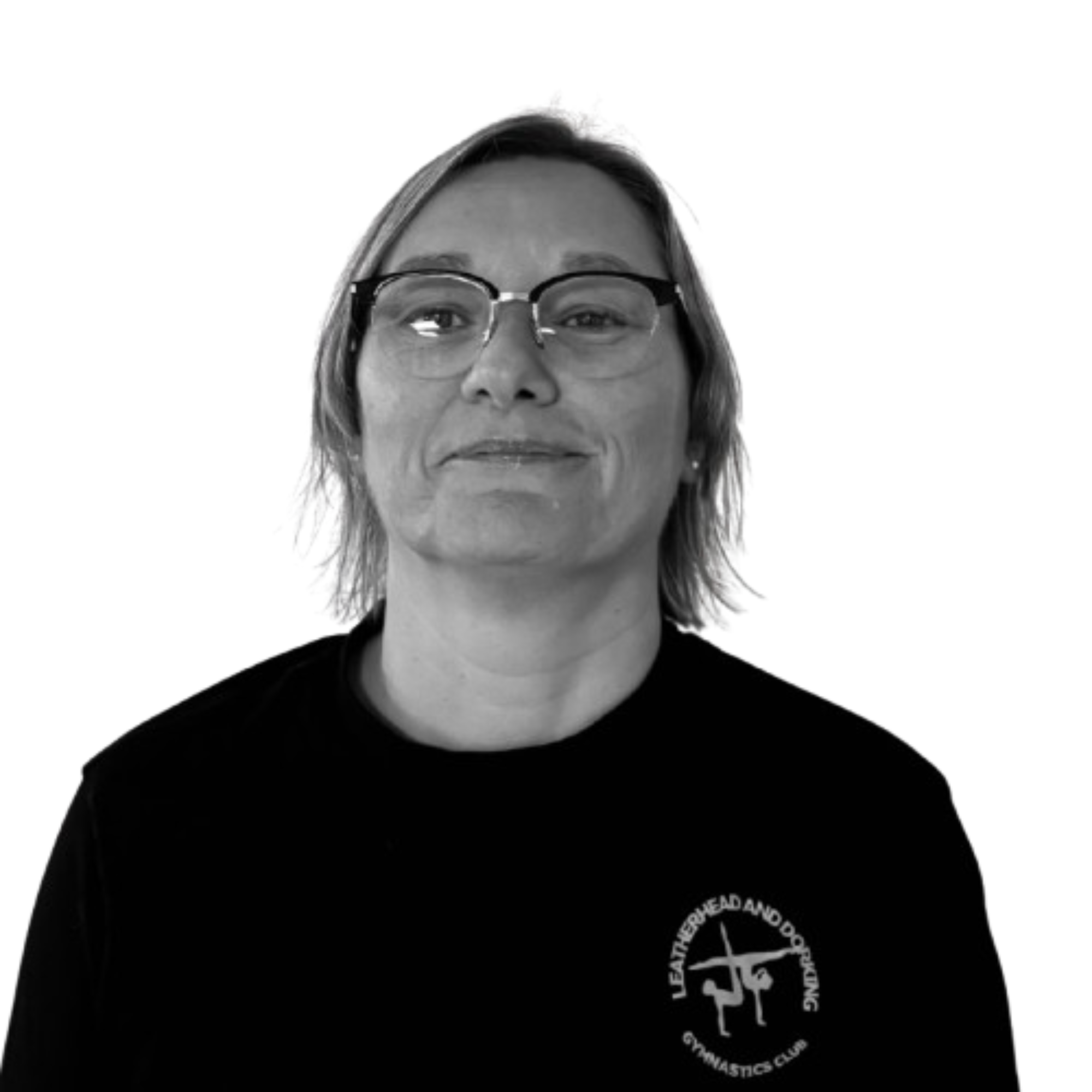 Close-up of a woman's face with glasses, wearing a black shirt with white circular emblem and text, against a plain background.