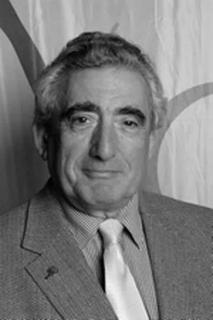 Black and white portrait of a man in a suit and tie, standing in front of a curtain.