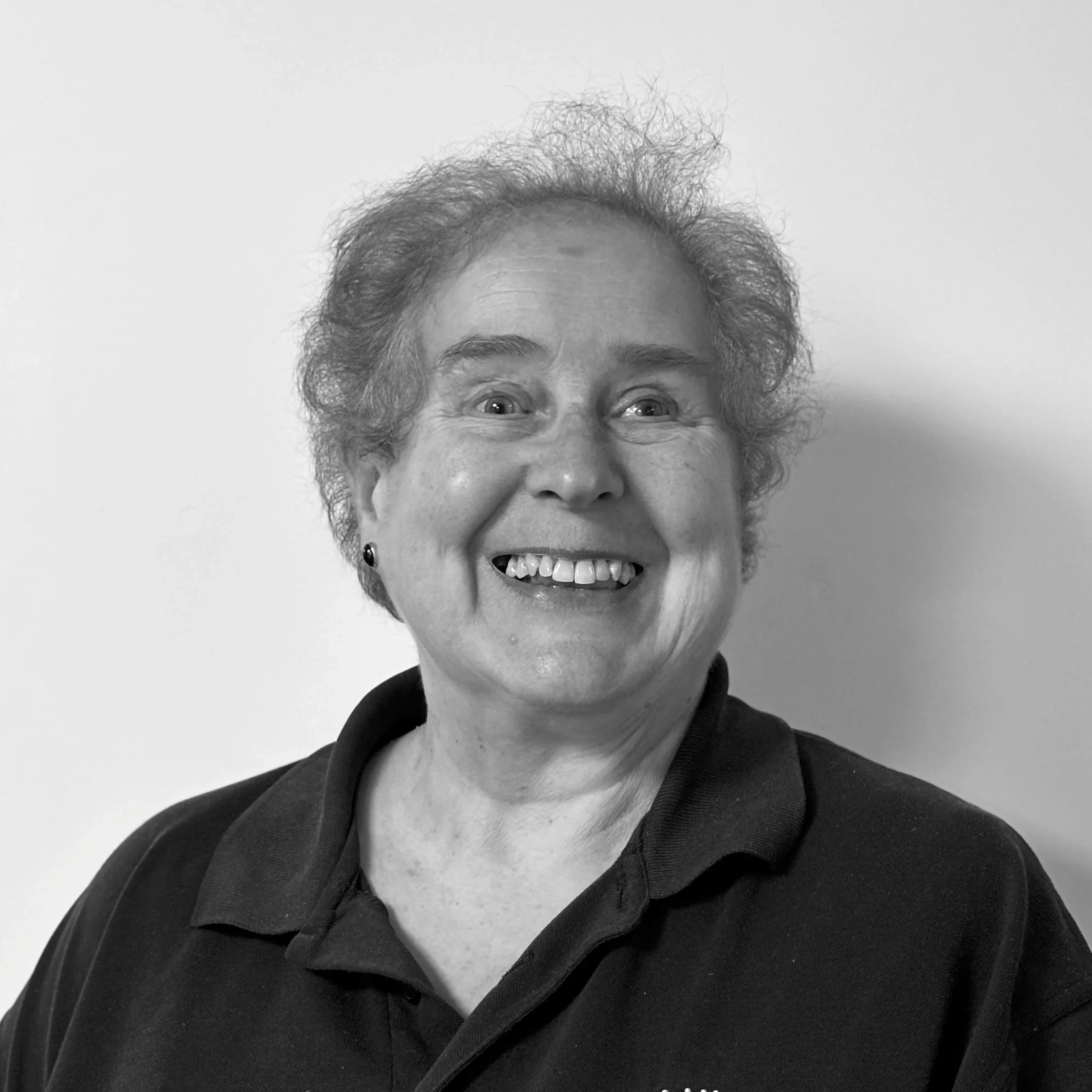 Close-up black-and-white photo of an elderly woman's smiling face, showing her eyes, nose, mouth, and curly hair.
