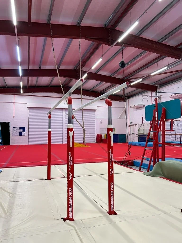 Indoor gymnastics training area with parallel bars, a springboard, and mats, in a gym with a red and white color scheme.