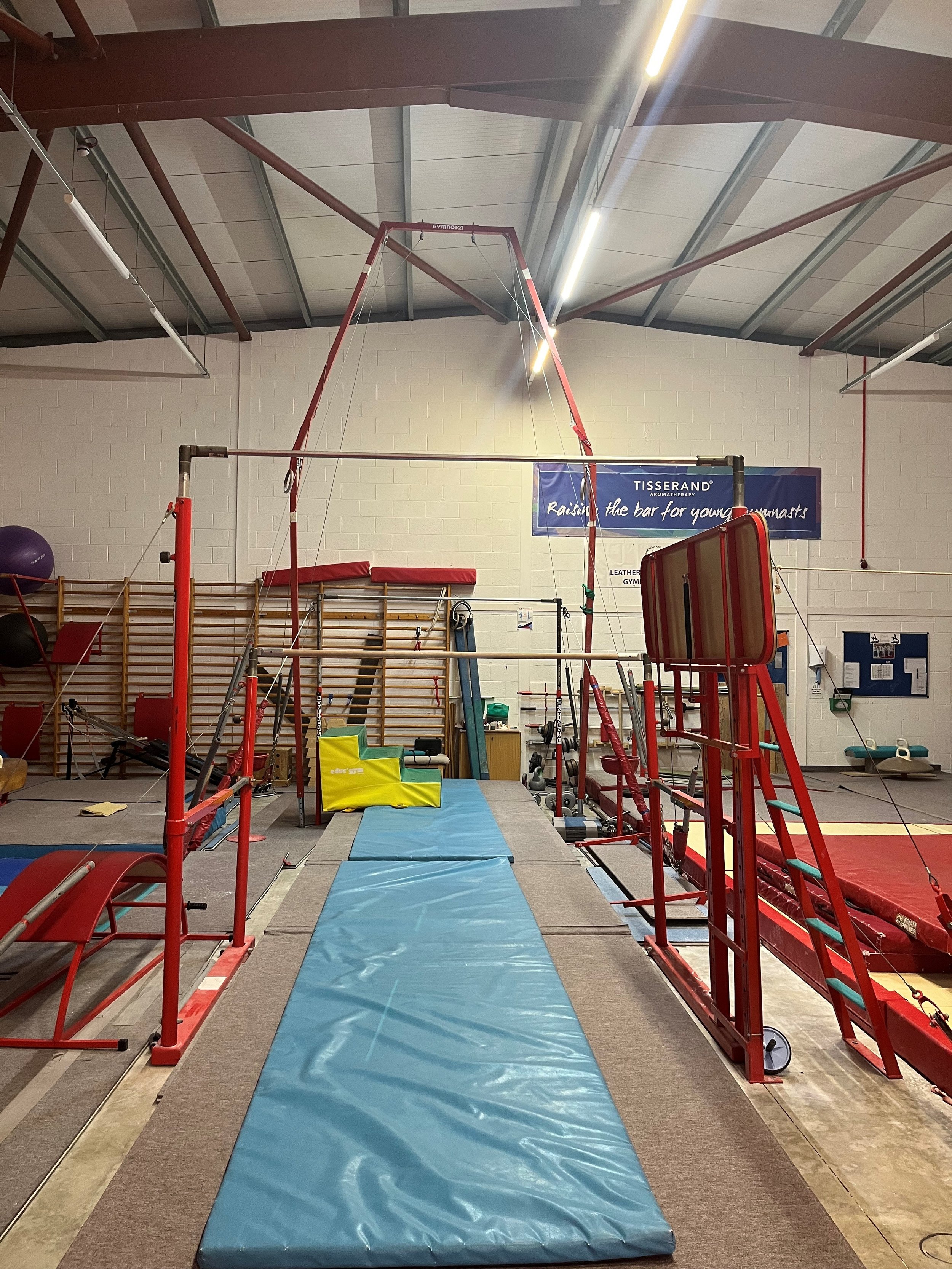 Indoor gymnasium with gymnastics equipment including a pommel horse, mats, and a high bar, set up for training or practice.