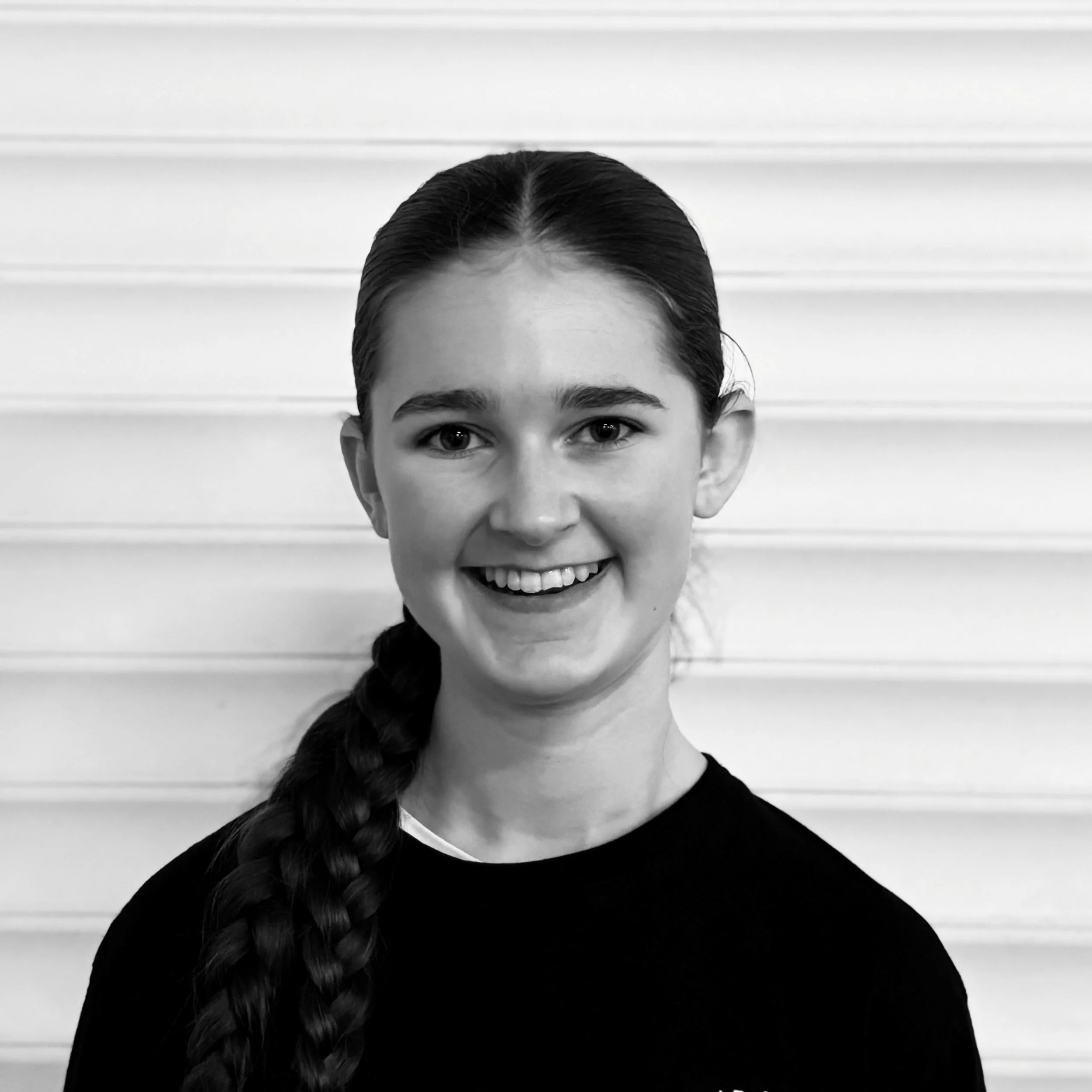 Black and white photo of a person with dark hair styled in a braid, smiling with visible teeth, against a horizontal striped background.