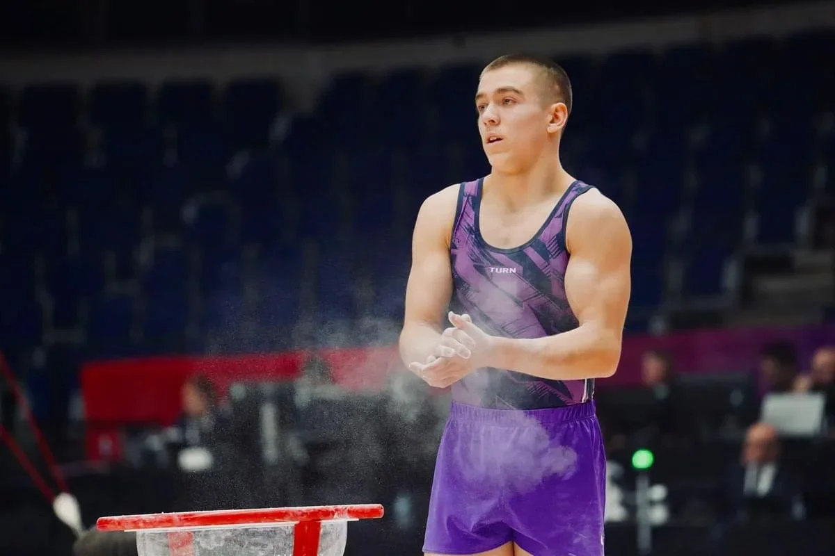 A male gymnast clapping his hands during a competition, with chalk dust in the air, standing near a red chalk trapezoid.