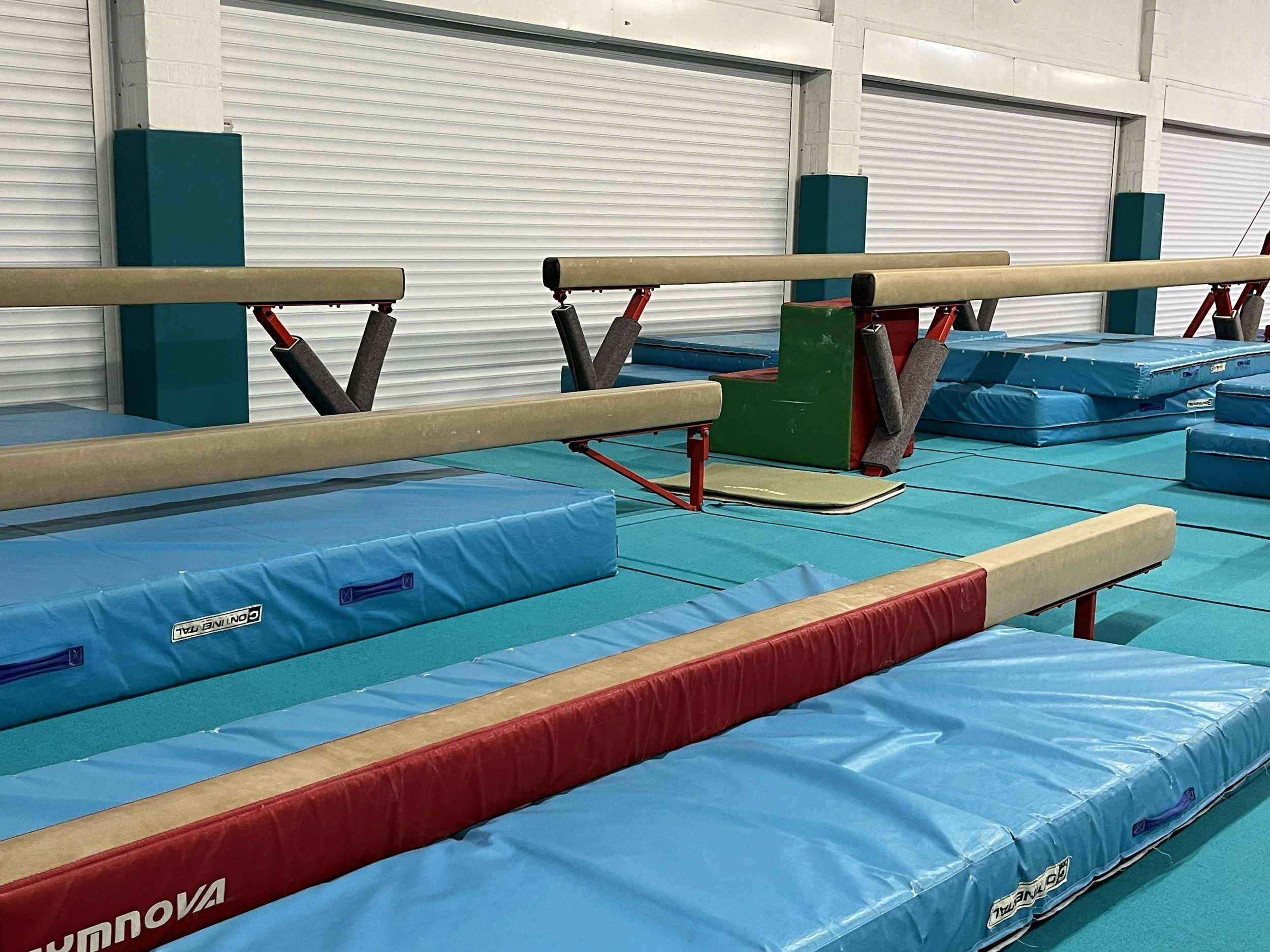 Gymnastics training area with padded mats and uneven bars in an indoor gym.