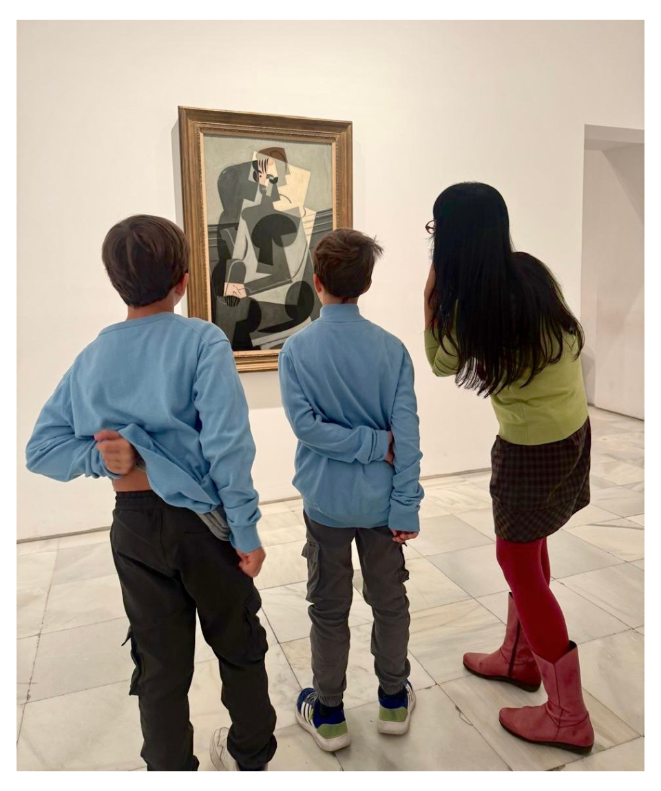 Three children and a woman observe a cubist-style abstract painting in a gallery.