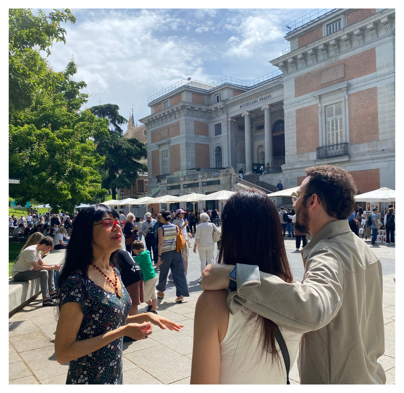 People gathered outside the Museo del Prado in Madrid, with a historic building in the background and a partly cloudy sky.