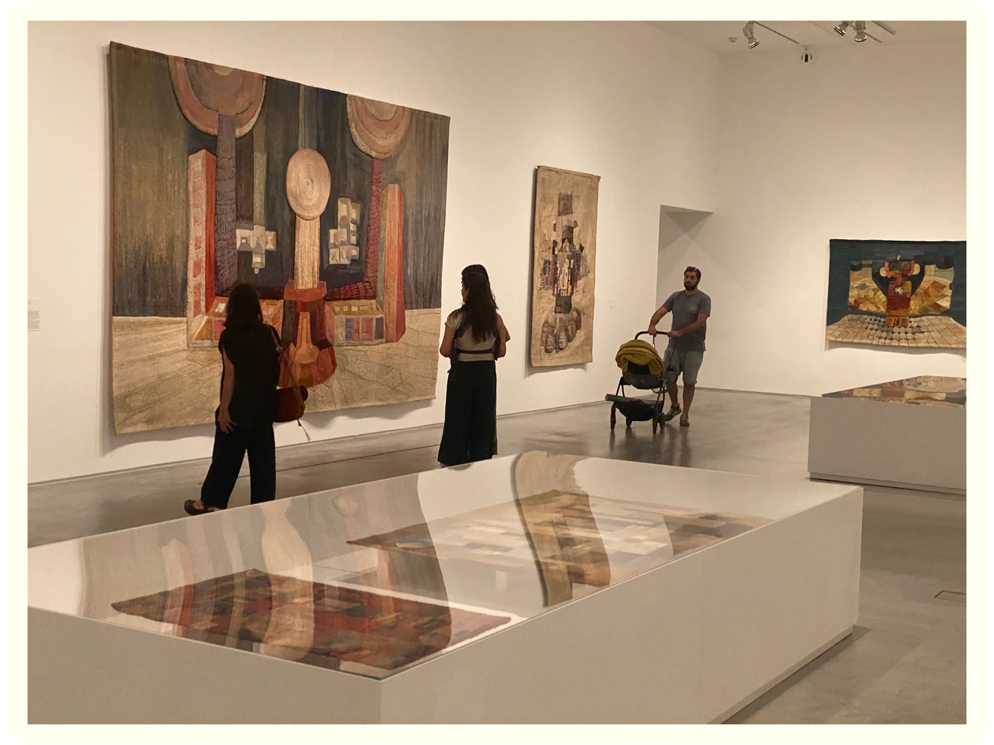 People inside an art gallery observing colorful abstract and geometric paintings on the wall.