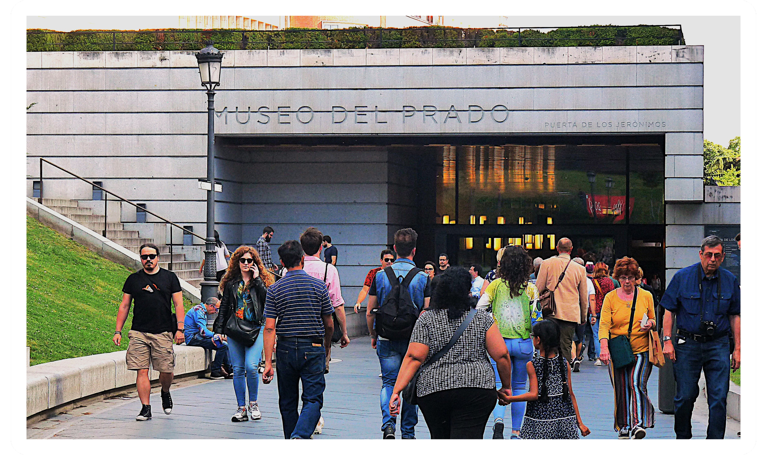 People walking outside of the Museo del Prado, with some crossing a street and others walking on the sidewalk, in Madrid, Spain.