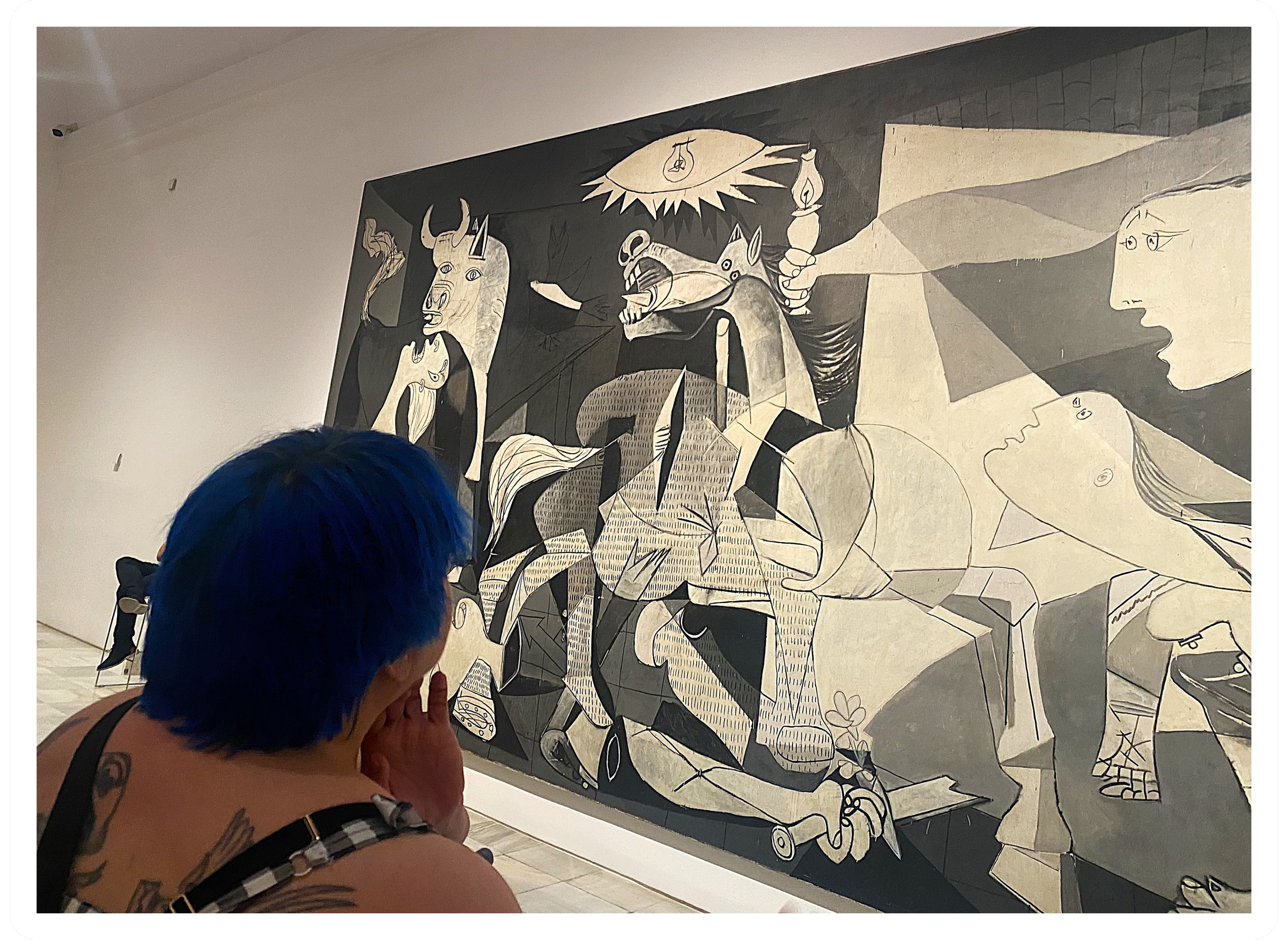Person with blue hair looking at a black-and-white abstract mural in an art gallery.