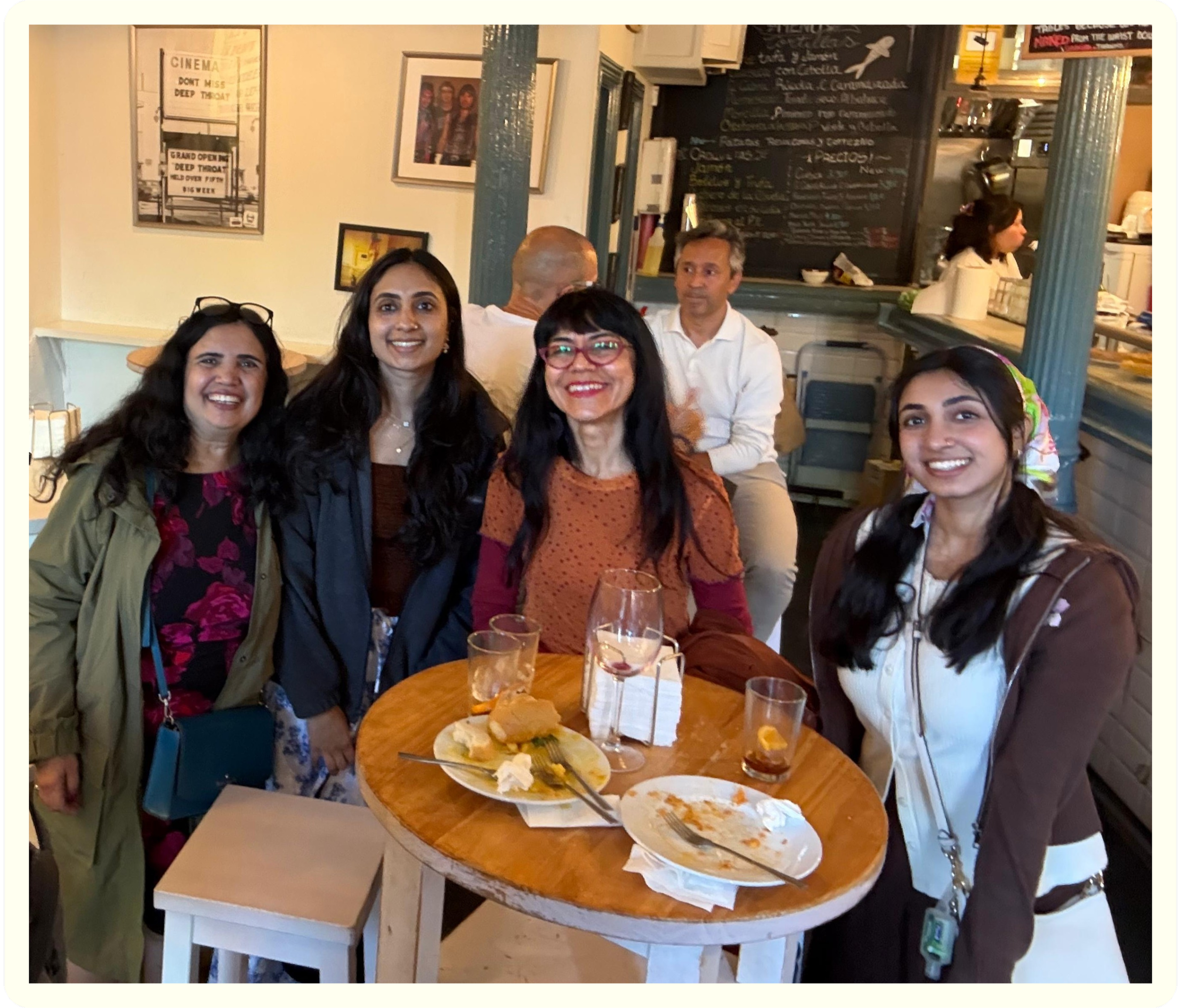 Group of five people smiling around a wooden table with food and drinks in a restaurant.