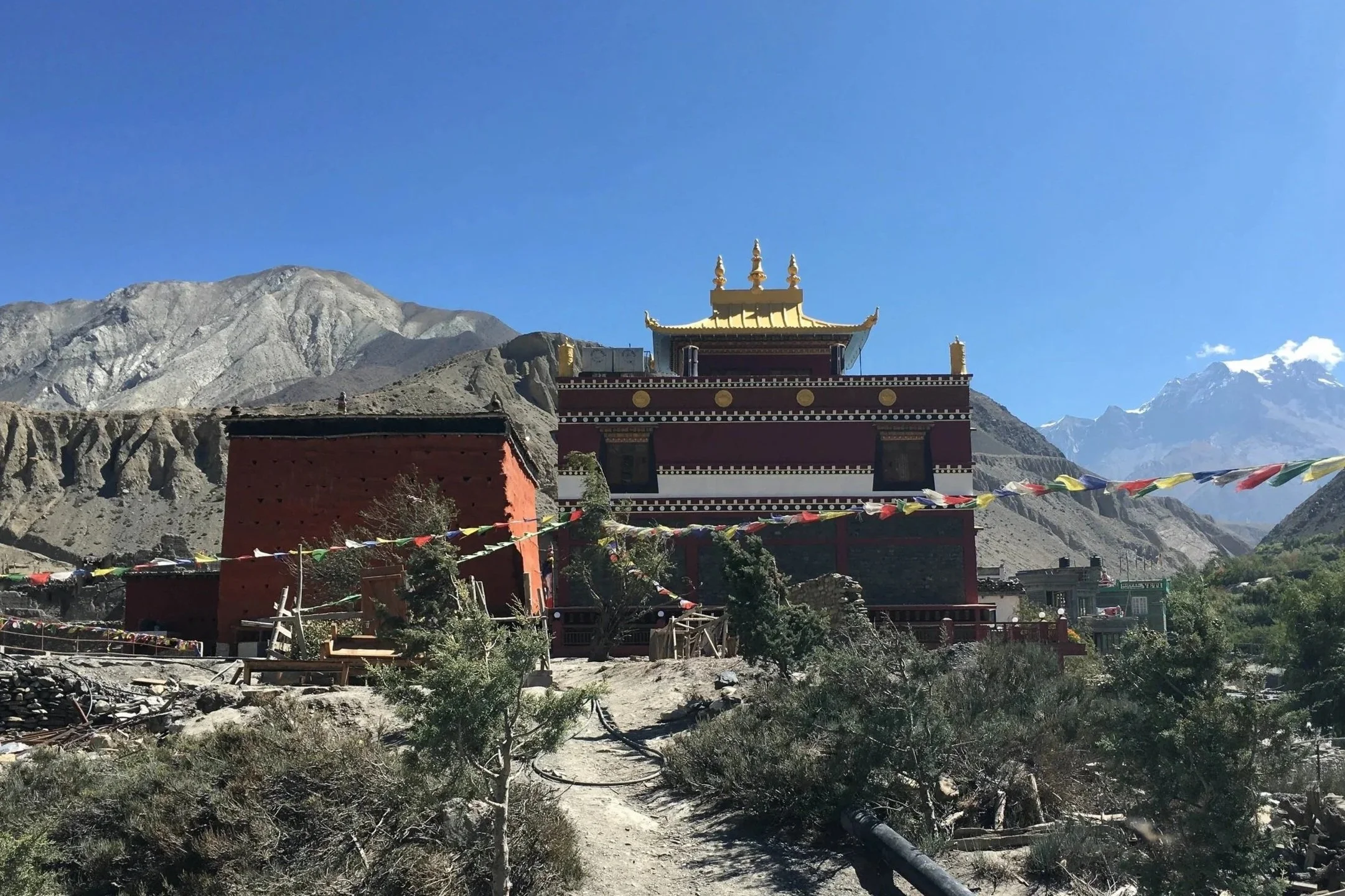 Mountain landscape with a temple in the foreground, decorated with prayer flags, mountains in the background, and a clear blue sky.