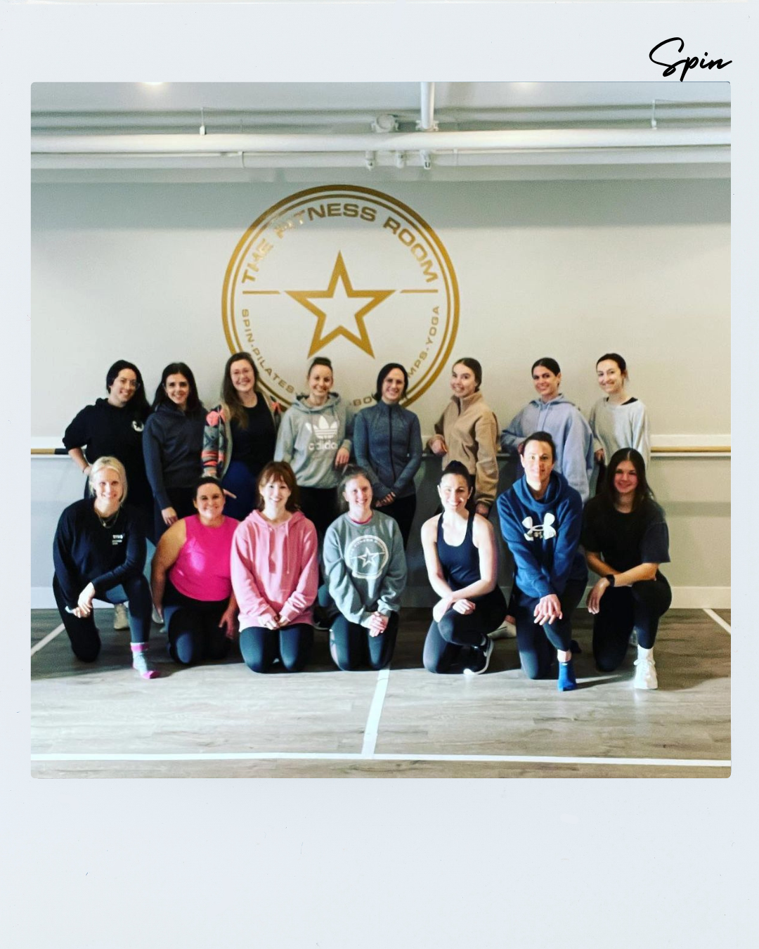 Group of women in workout clothing posing inside a fitness room with a large star logo and text on the wall that reads 'The Fitness Room'.