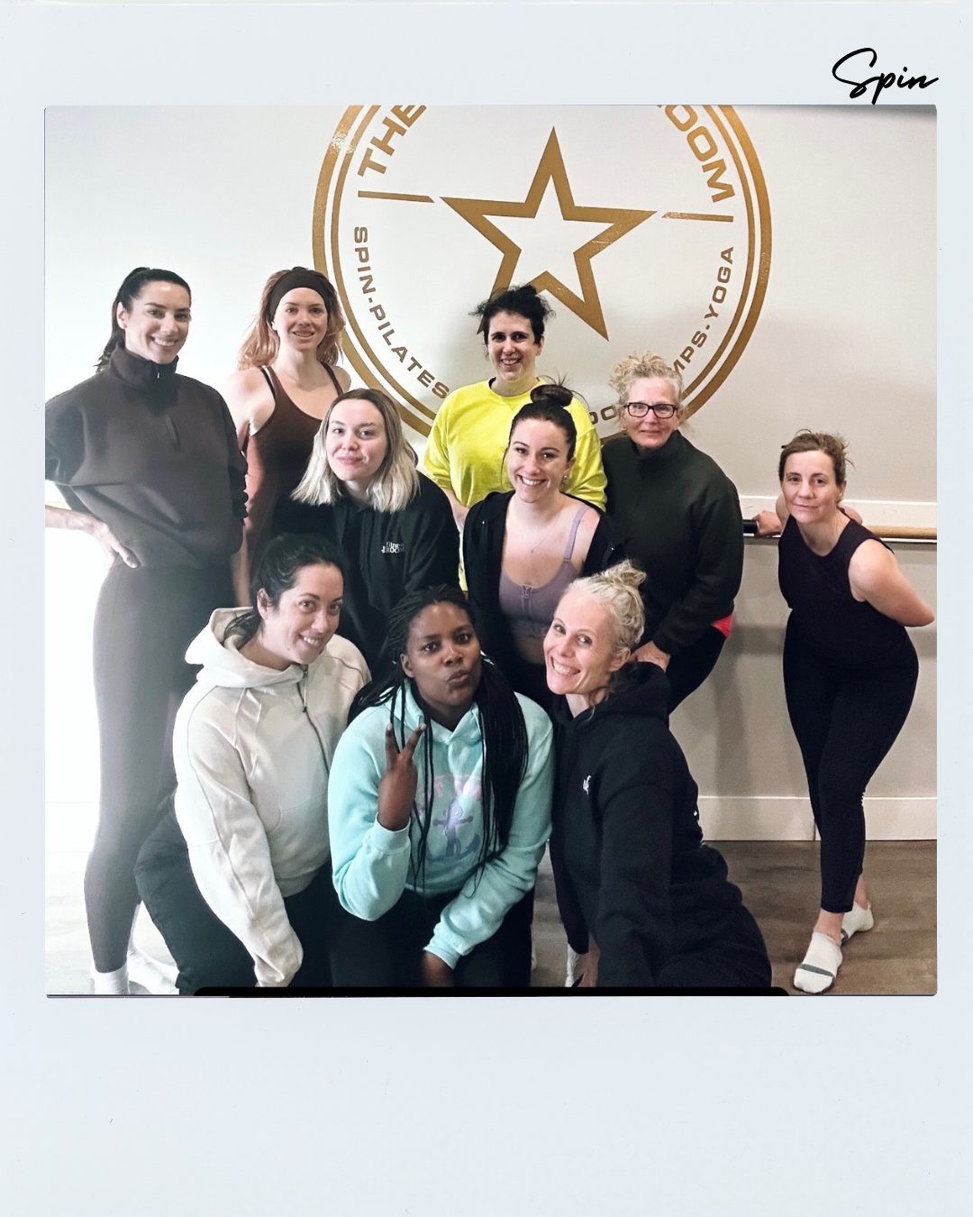 Group of ten women posing in front of a wall with a logo featuring a star and text, inside a frame that says 'Spin' in the top right corner.