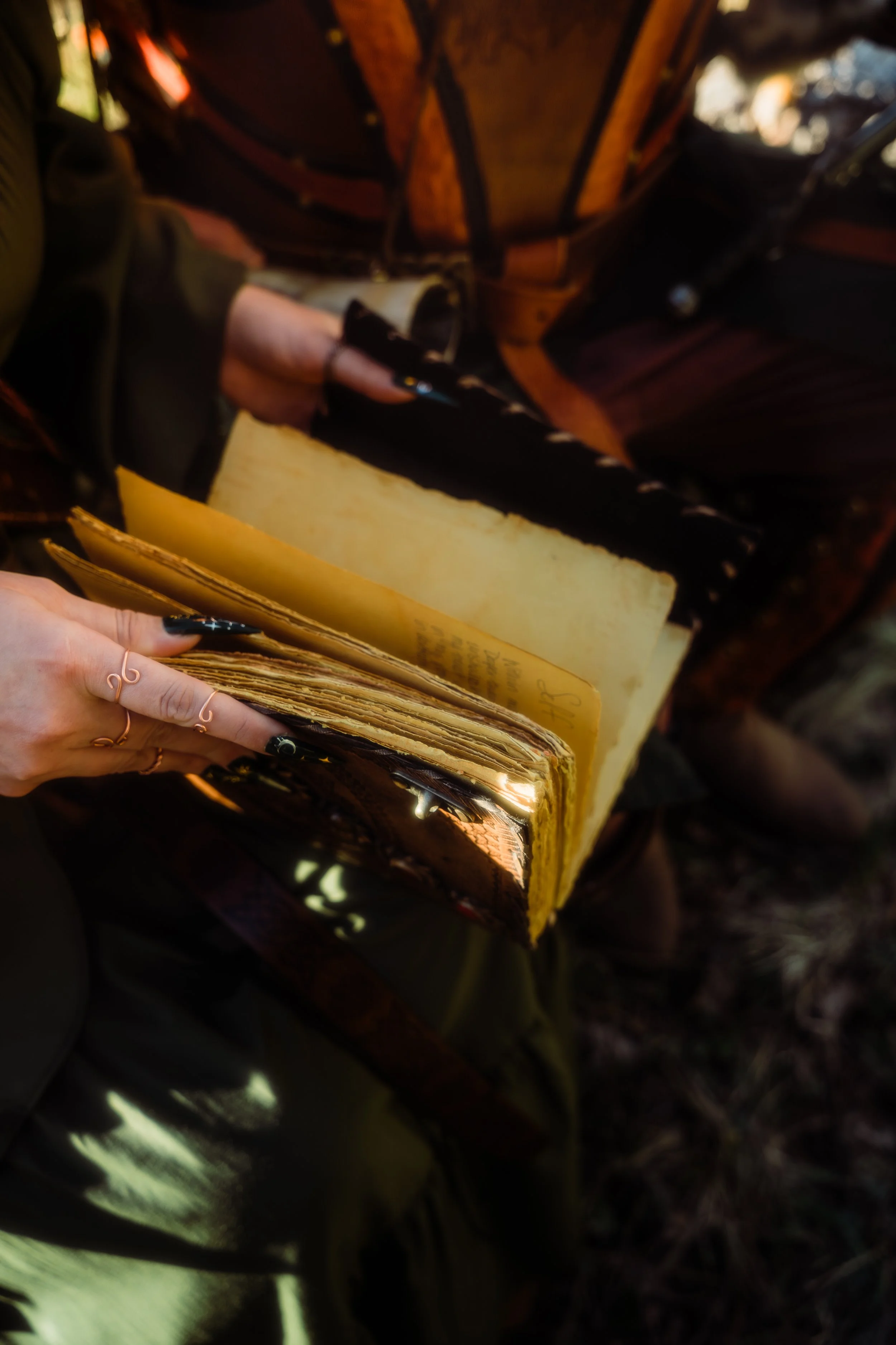 A person holding a vintage leather suitcase and an old notebook or journal near some leaves and trees.