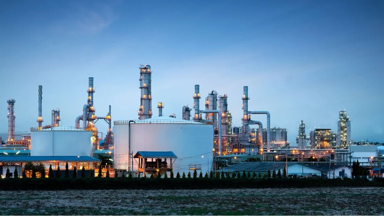 An industrial oil refinery with multiple towers and pipes illuminated at dusk.