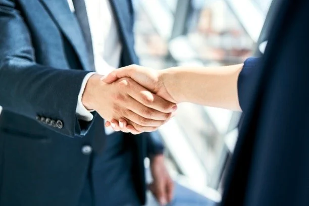 Close-up of two people in business suits shaking hands in a modern office setting.