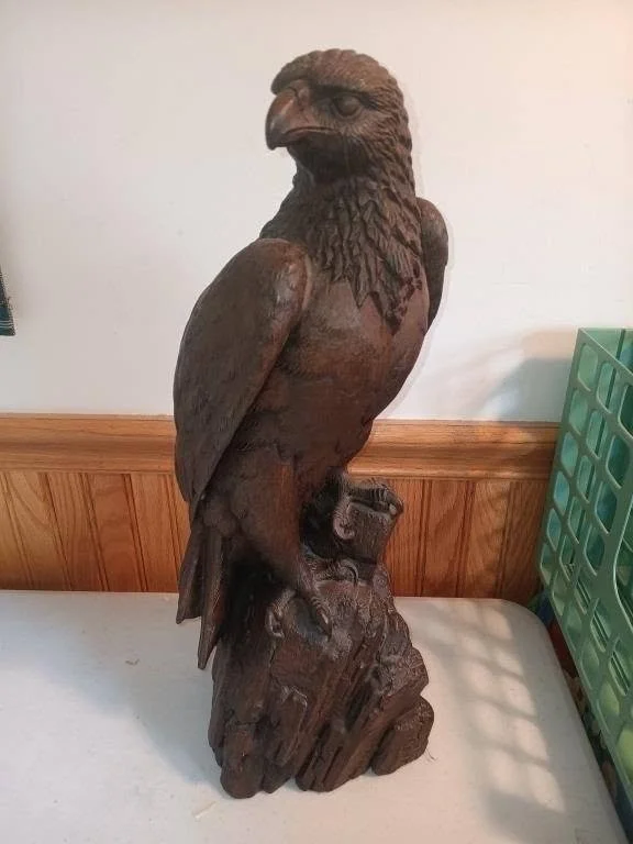 Wooden carved eagle statue perched on a stump with detailed feather and talon carving.