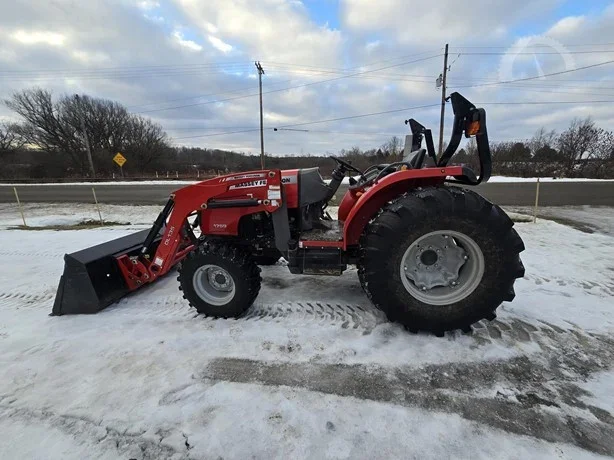 Red compact tractor with front loader attachment on snowy ground, parked near a road.