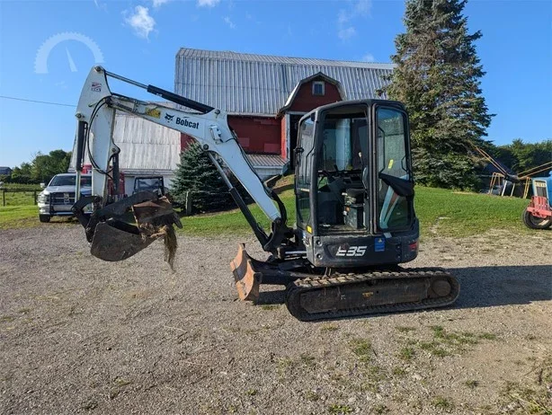 Bobcat E35 mini excavator on a gravel surface with a red barn and trees in the background.