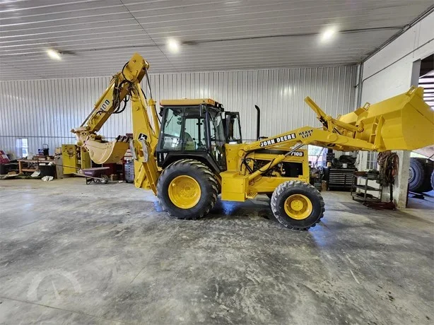Yellow John Deere backhoe loader inside a warehouse, with tools and equipment in the background.
