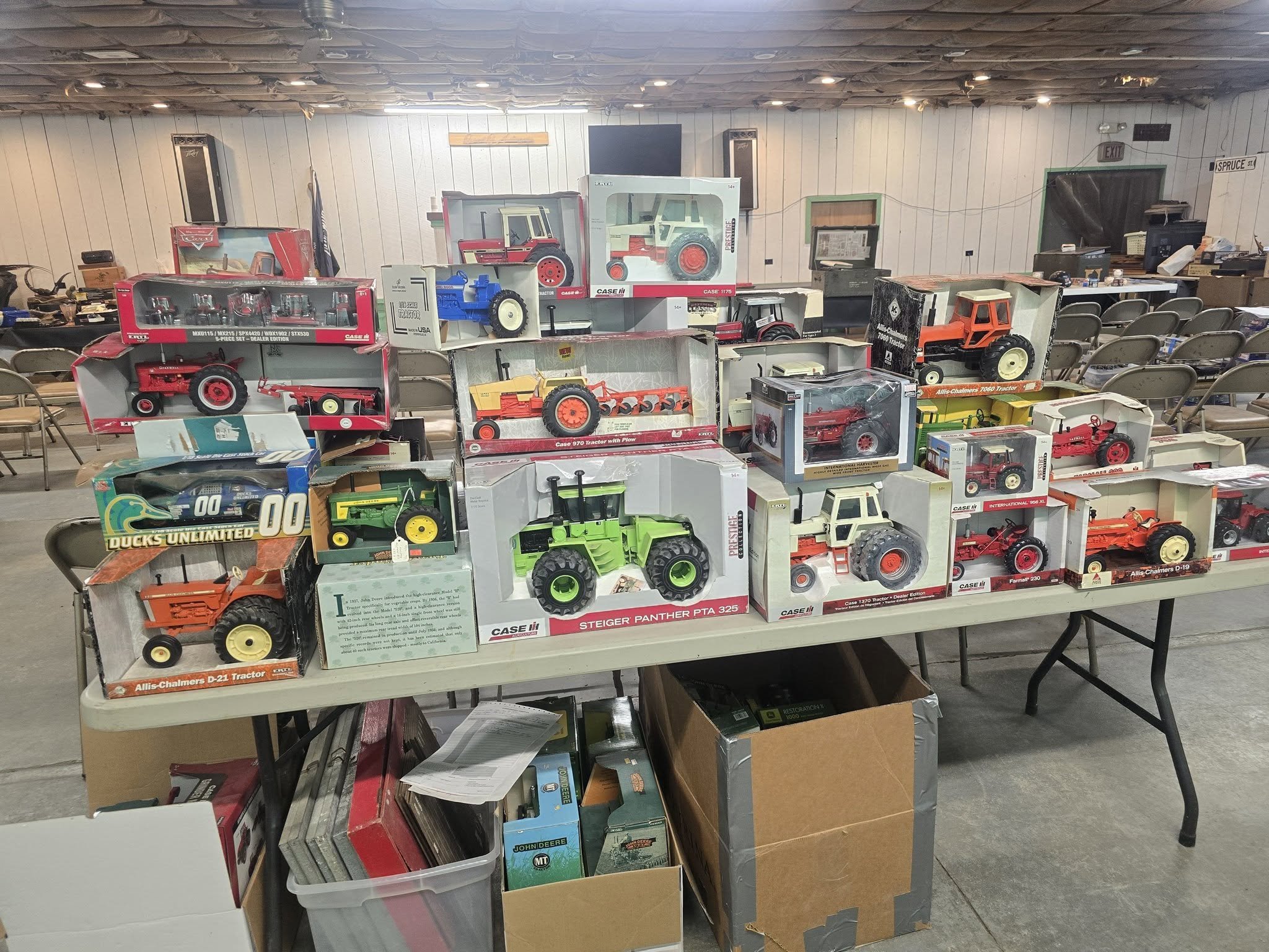 Collection of boxed die-cast farm toy tractors and equipment displayed on an auction table.