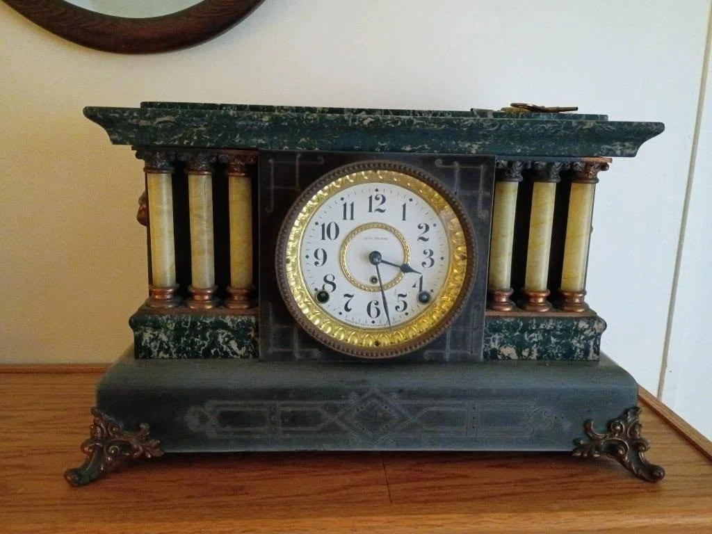 Antique mantel clock with decorative columns, brass trim, and a white clock face.
