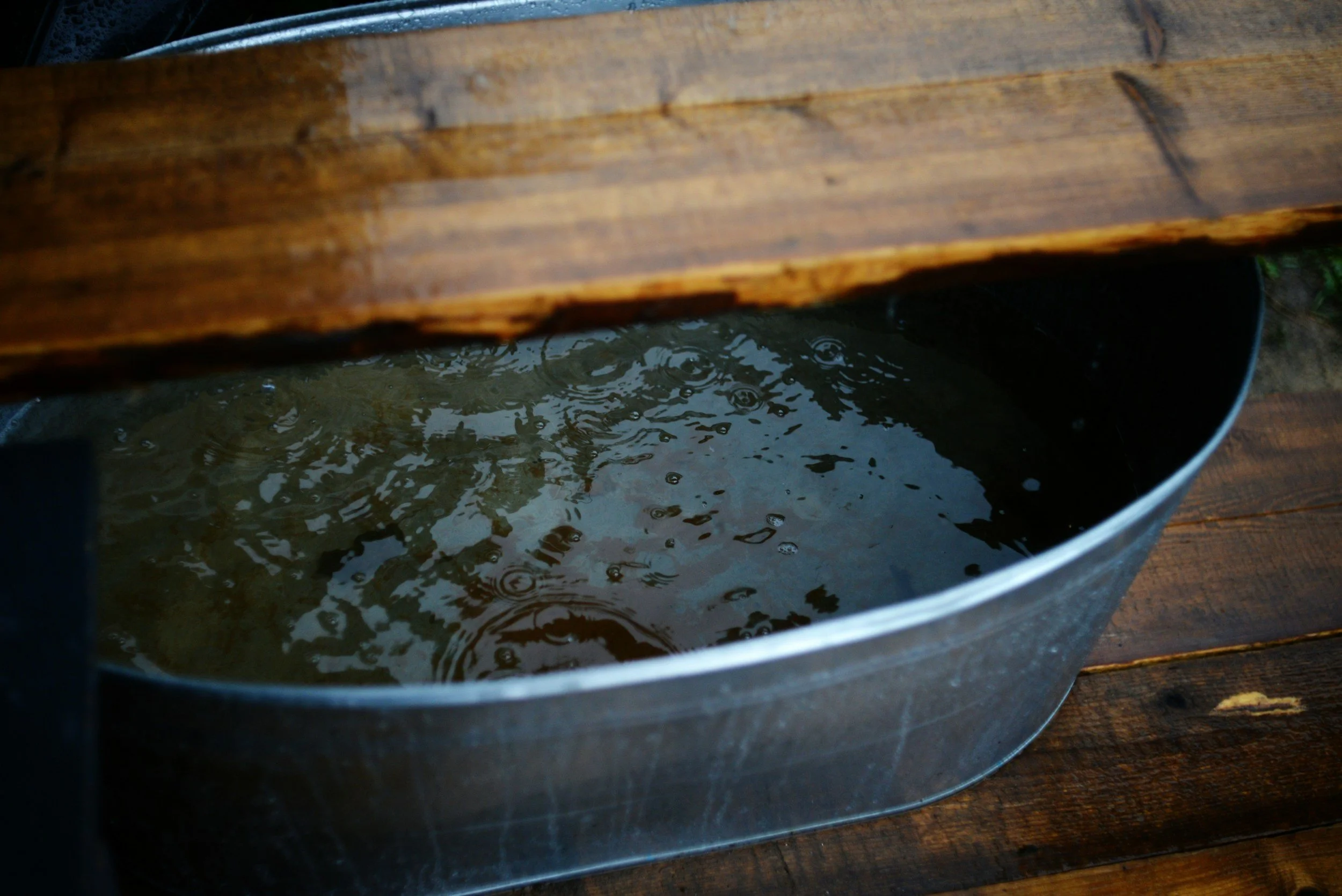 A bucket filled with water placed underneath a wooden structure with water droplets on it.