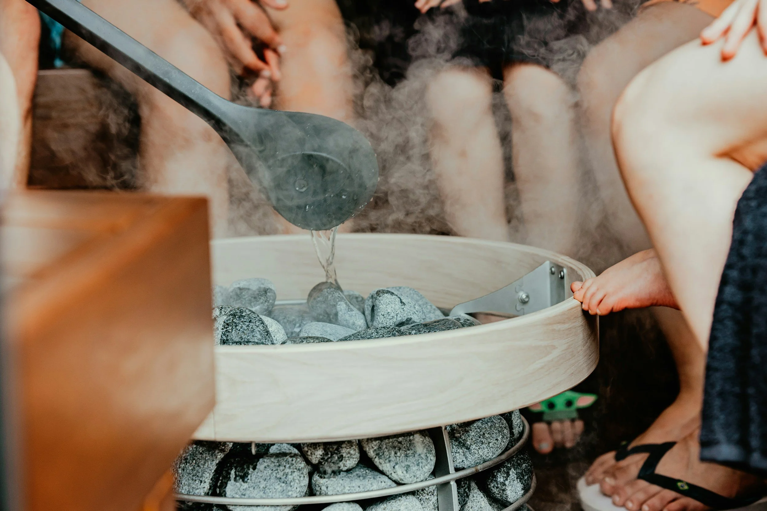 Kids gathered around a steam sauna or bath with rocks and a wood bucket, enjoying a relaxing scene.