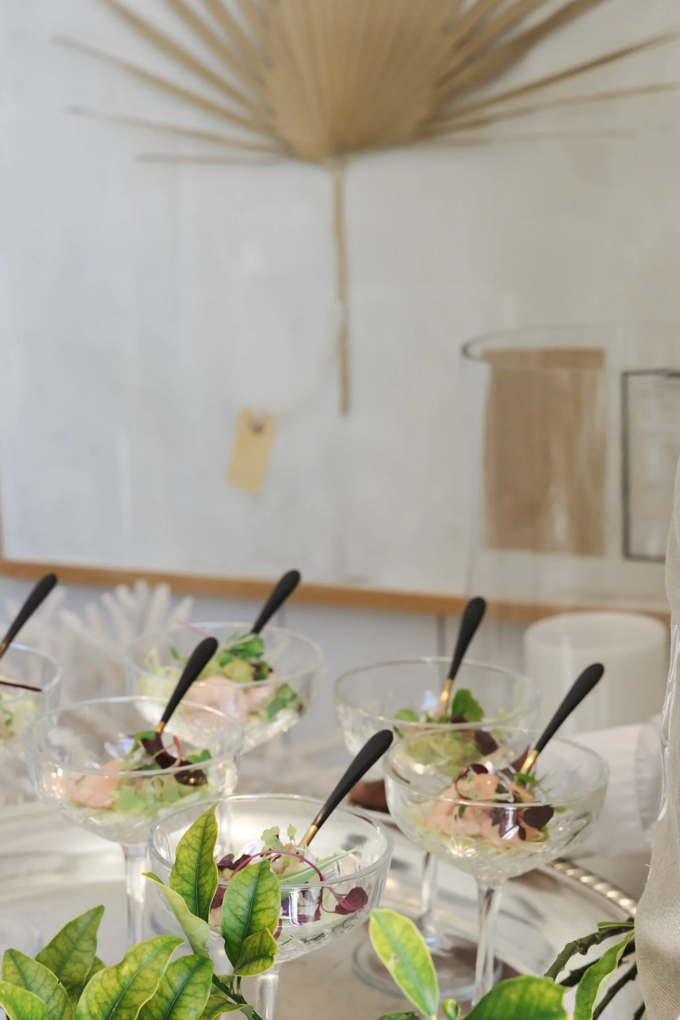 Multiple glass dessert cups filled with salad, garnished with fresh herbs, displayed on a white table at an event.