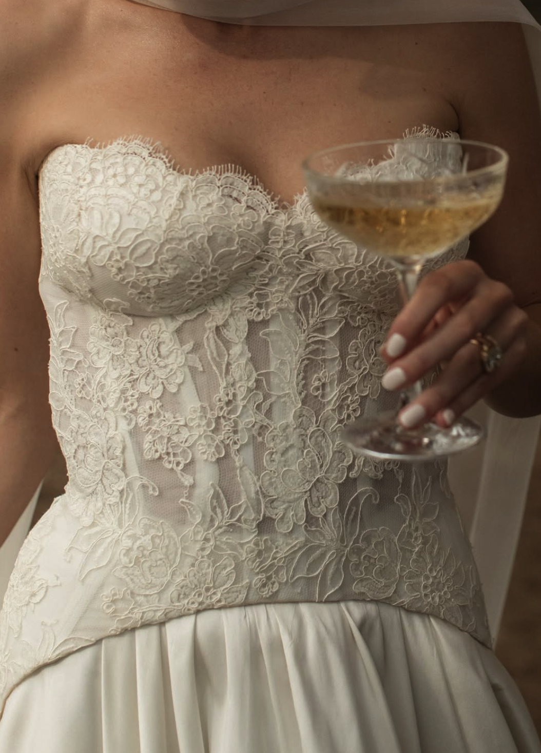 Close-up of a woman in a white lace wedding dress holding a glass of champagne.