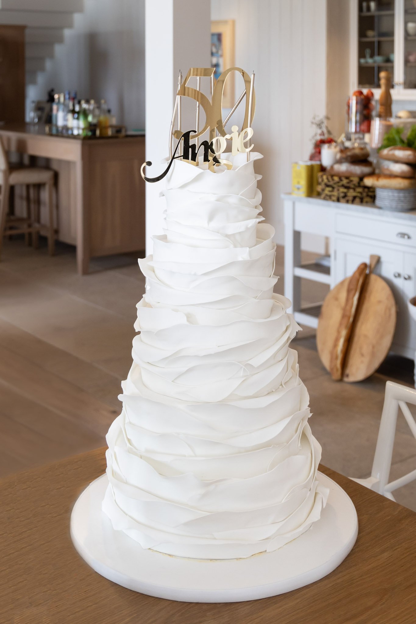A white wedding cake with a gold "50" topper and the name "Amie" in black script.