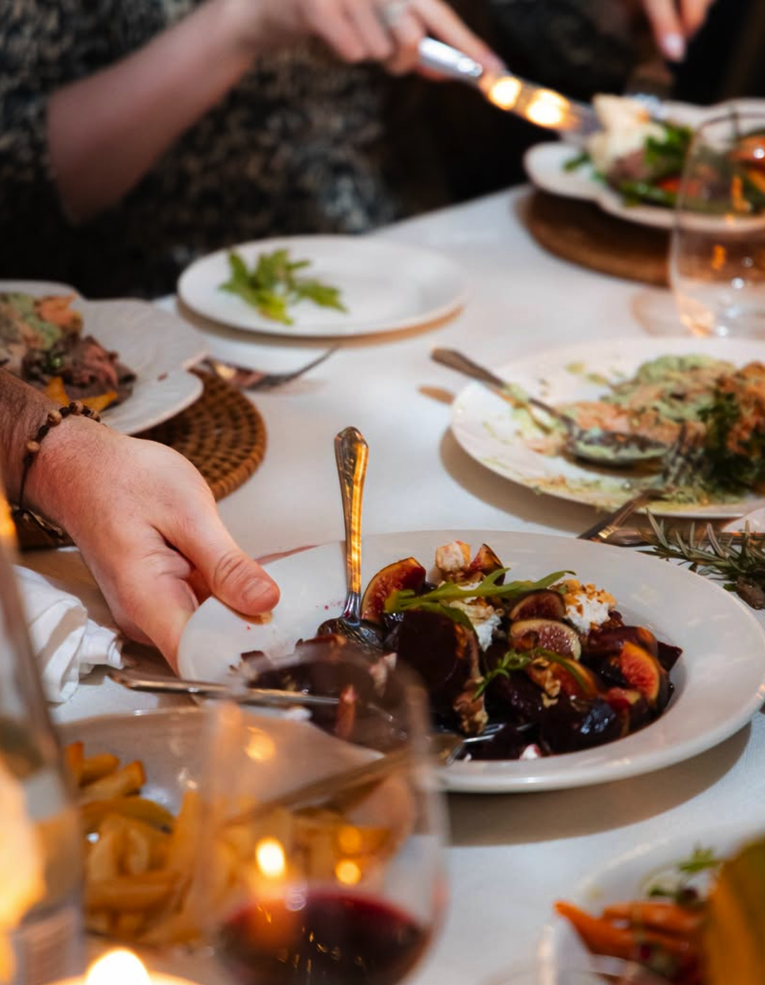 People sharing a meal with plates of food, glasses of red wine, and a table decorated for a gathering.