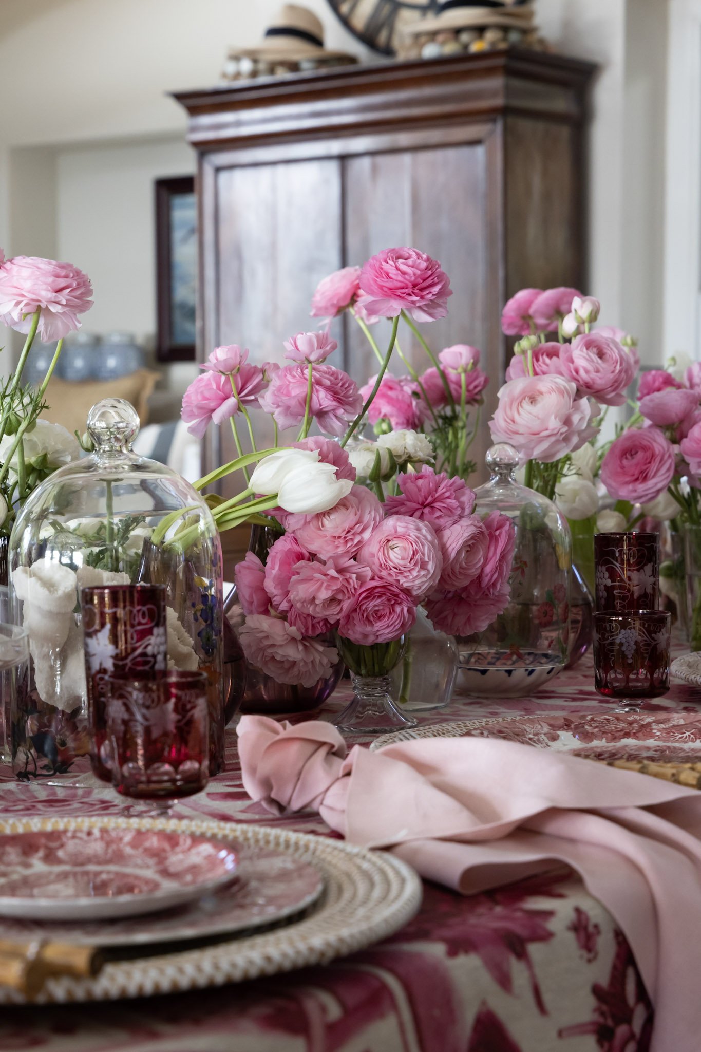 A table decorated with pink flowers, glass bowls, and red and white patterned tableware, set for a meal in a cozy, well-lit room.