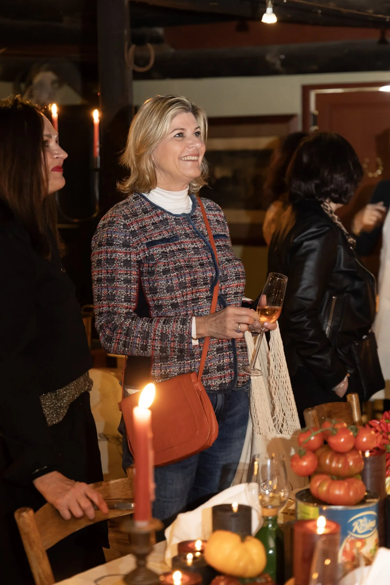 People gathered around a table during a celebration, with candles, tomatoes, and drinks, in a warmly lit room.