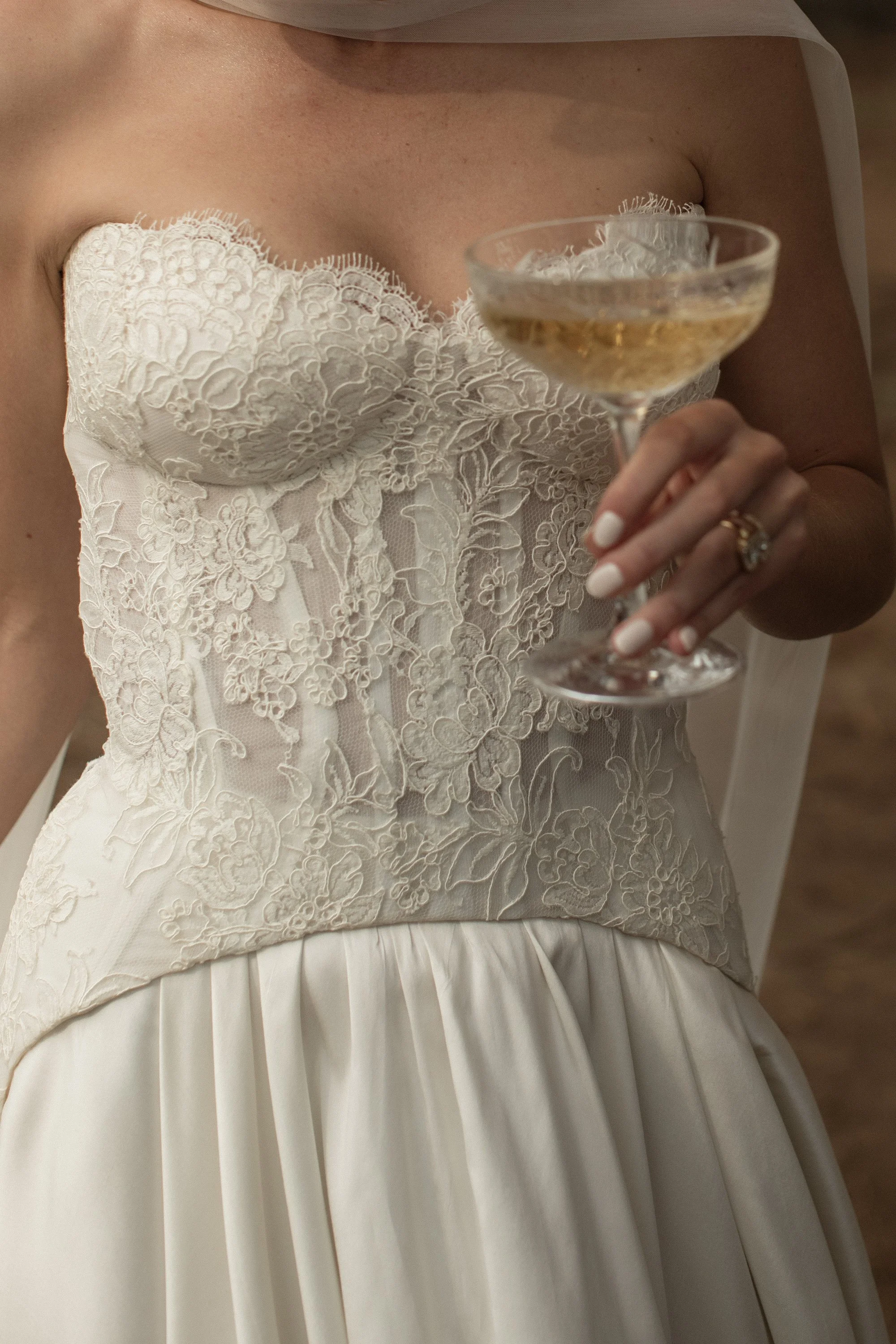 Close-up of a woman in a wedding dress holding a champagne glass, focusing on the intricate lace details of the dress.