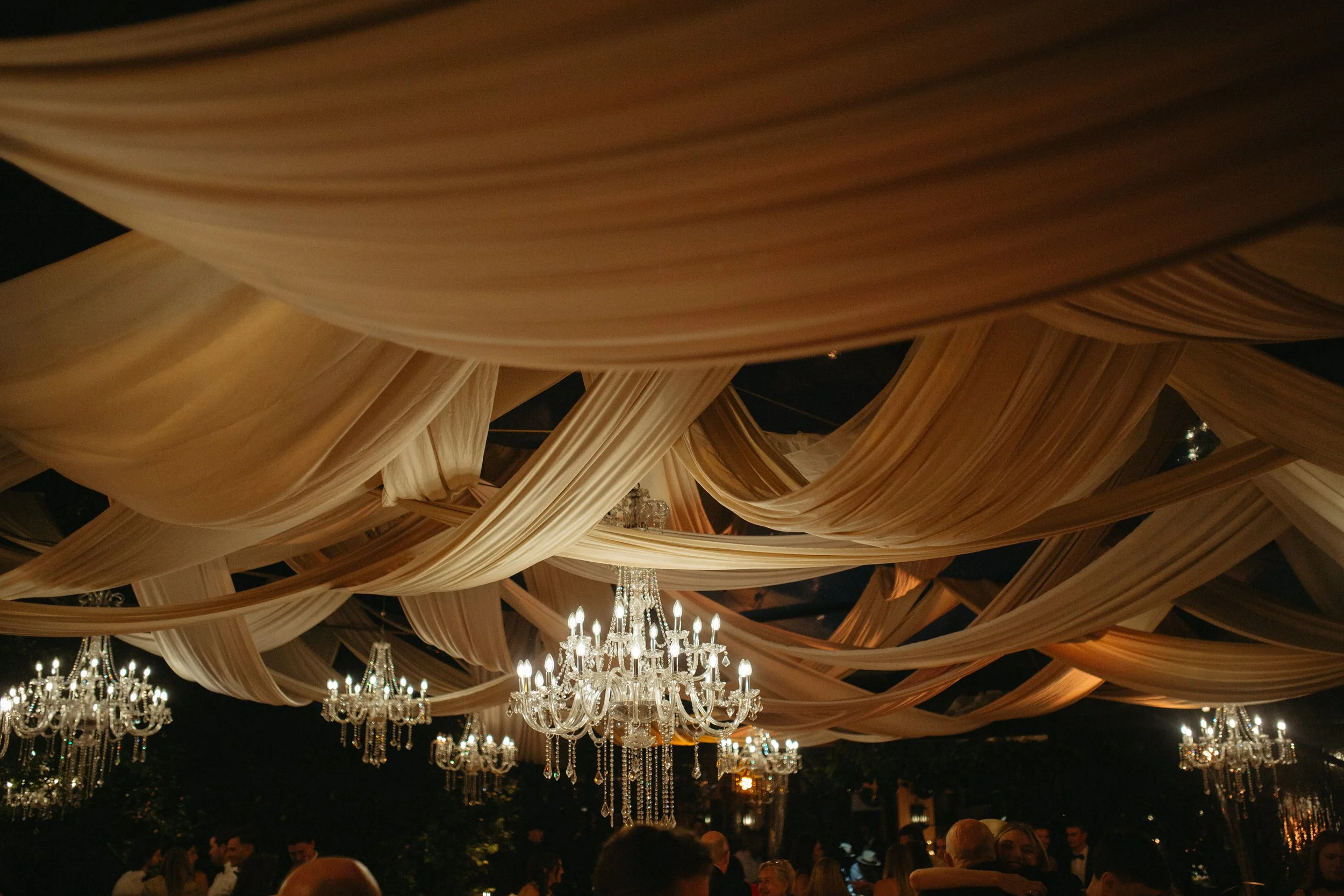Elegant ceiling drapery with chandeliers and guests at a formal event.