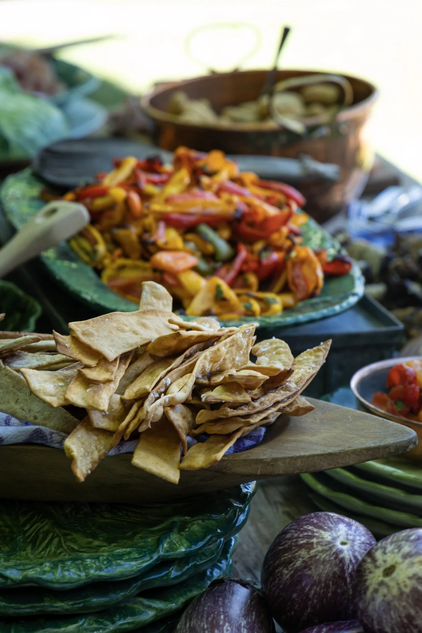 A variety of colorful food items, including stacked flatbread, pasta salad with vegetables, and figs, displayed on a table, likely at a market or food event.